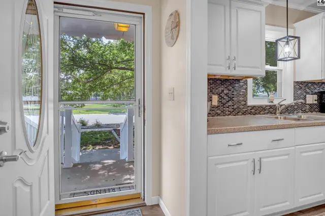 Bright kitchen with white cabinets and mosaic backsplash, viewed from entryway with porch visible through screen door.