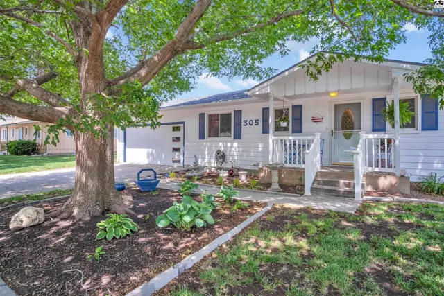 Charming white ranch home with blue shutters, a covered porch, and mature tree in the front yard.