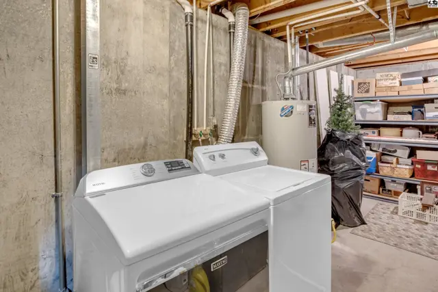 Laundry area with white washer and dryer, concrete walls, and storage shelves.