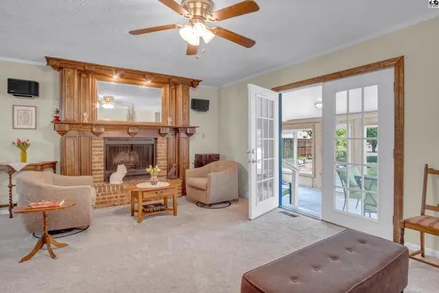 Living room with brick fireplace, wood mantel, ceiling fan, and French doors opening to a sunroom.