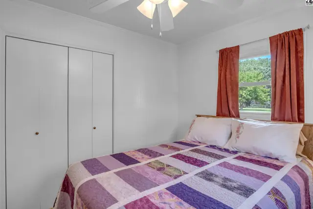 Bedroom with a white ceiling fan, white closet doors, and a colorful quilt on the bed.