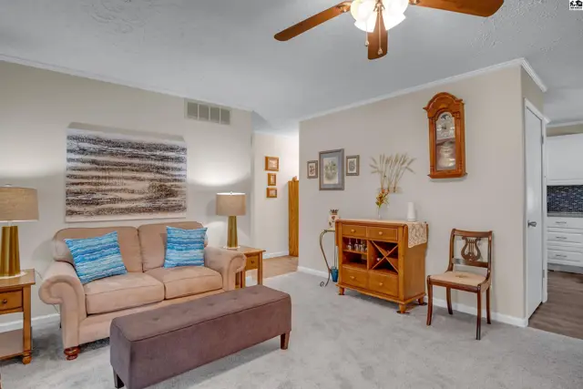 Cozy living room with beige sofa, brown ottoman, wood cabinet, and neutral carpet.