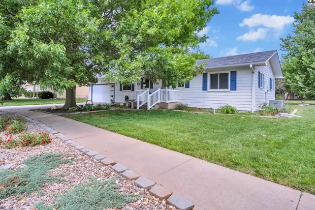 White ranch home with blue shutters, white railing, and mature trees on a sunny day.