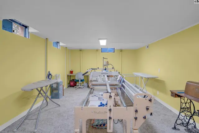 Spacious room with quilting machine, ironing boards, and sewing machine on a gray floor.