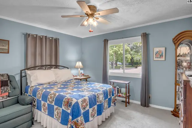 Light blue bedroom with a queen bed, quilted comforter, and a grandfather clock.