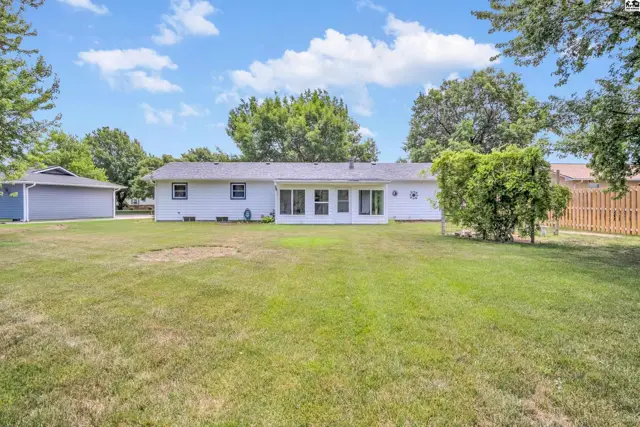 White ranch home with a sunroom addition, large backyard, and detached garage.