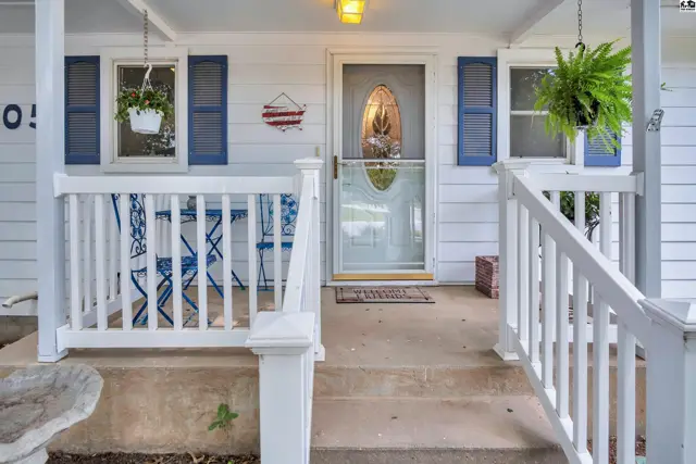 White porch with blue shutters, white railings, and a glass-paneled front door.