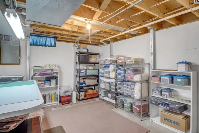 Unfinished basement with exposed joists, white walls, and ample storage shelving filled with bins.