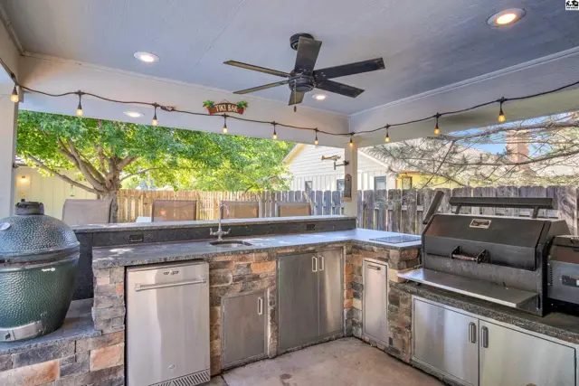 Covered outdoor kitchen features stone base, granite counters, grill, and stainless steel appliances.