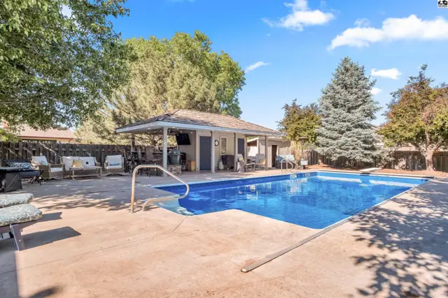 Spacious backyard with a large blue swimming pool, concrete patio, and covered outdoor entertainment area.