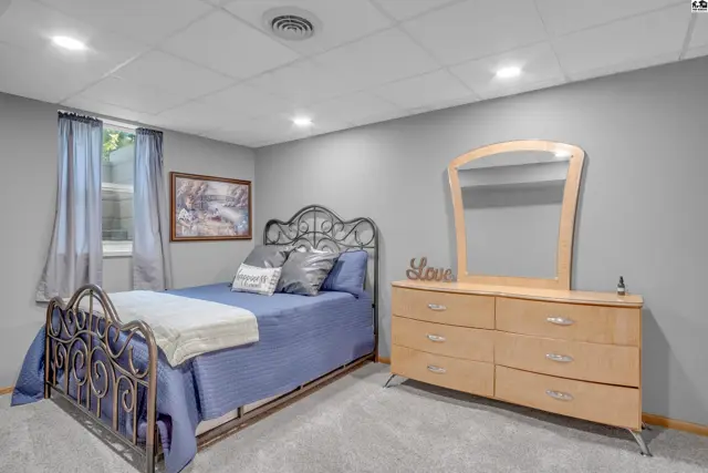 Bedroom with a black metal bed frame, blue bedding, and a light wood dresser with mirror.