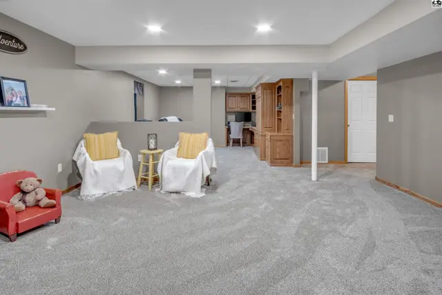 Spacious finished basement with gray carpet, two chairs, and built-in wooden cabinetry.