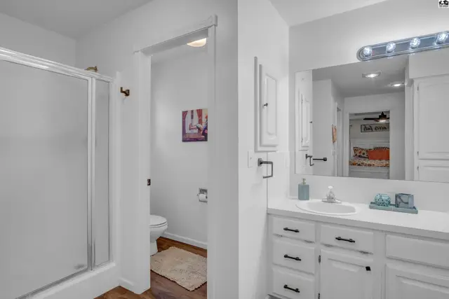 Bright white bathroom with a glass shower, vanity, and toilet visible through an open doorway.