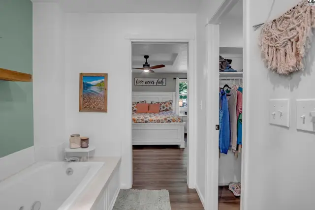 Bright bedroom with white furniture and a ceiling fan seen through an open doorway.