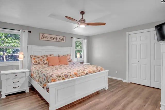 Spacious bedroom with a white paneled bed, floral bedding, and wood-look flooring.