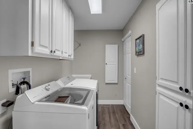 Spacious laundry room with white cabinets, a large white washer, and a tall white storage cabinet.