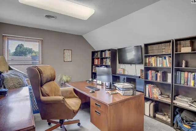 Spacious home office with a large desk, leather chair, and extensive built-in bookshelves.