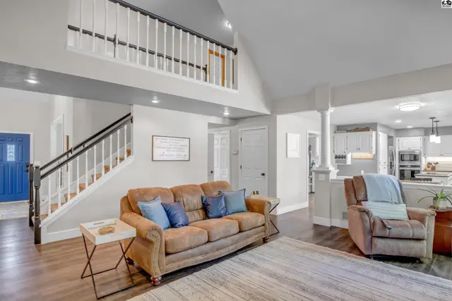 Spacious living room with a brown leather sofa, vaulted ceiling, and open staircase leading to a loft.