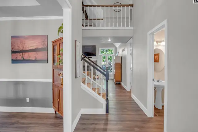 Spacious entryway with hardwood floors, a staircase with white railings, and a view into a living area.