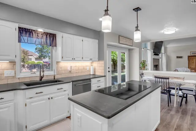 Modern white kitchen with a dark island, granite countertops, stainless steel appliances, and a breakfast nook.