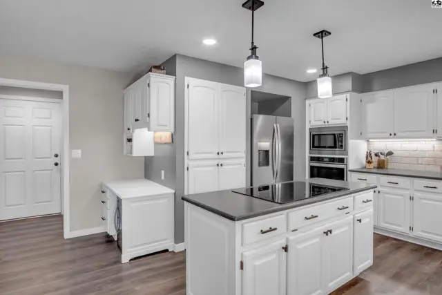 Spacious white kitchen with a large island, stainless steel appliances, and dark countertops.