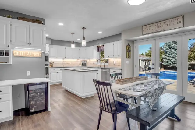 Spacious white kitchen with island, wine fridge, and dining area opening to a backyard pool.