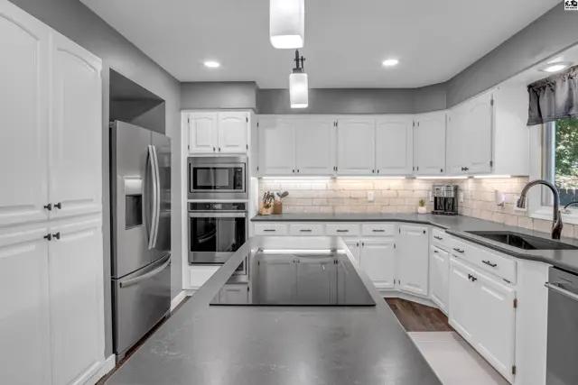 Spacious kitchen with white cabinets, stainless steel appliances, and a large gray island with a cooktop.