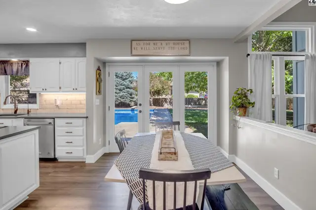 Dining area with a table set for meals, overlooking a backyard pool through French doors.
