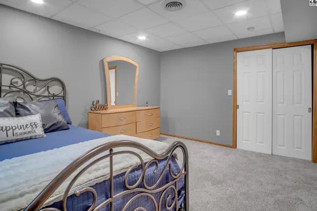 Spacious bedroom with gray walls, carpet, a metal bed frame, and a wooden dresser with mirror.