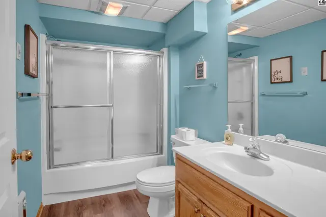 Bright blue bathroom with a white tub/shower combo, wooden vanity, and modern fixtures.