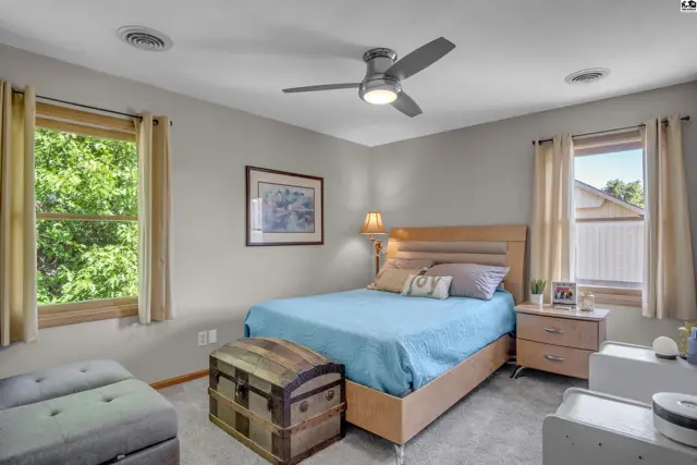Spacious bedroom with a light wood bed, blue bedding, antique trunk, and large windows.