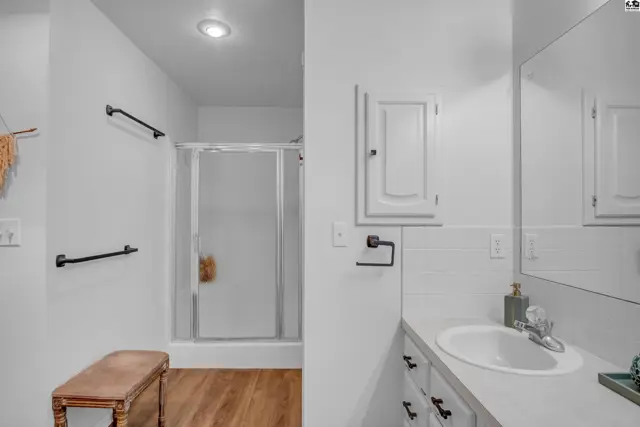 Bright bathroom with white tile, vanity, and glass-enclosed shower.