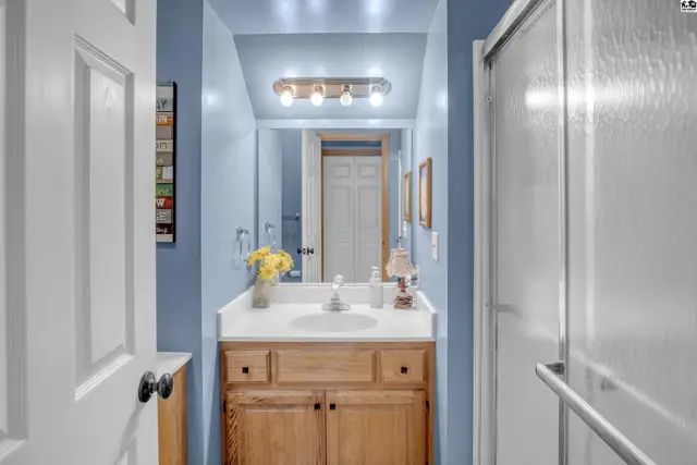 Light blue bathroom with a wooden vanity, white countertop, and glass shower stall.