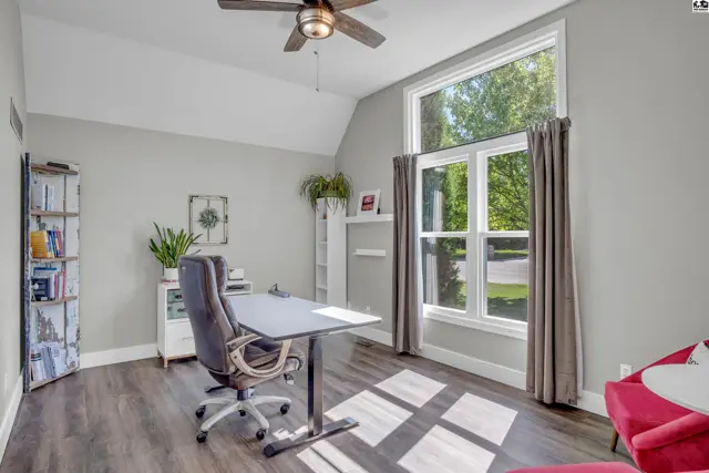 Bright home office with a large window, dark wood floors, and a ceiling fan.