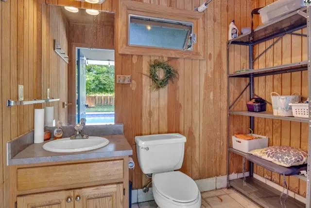 Rustic wood-paneled bathroom features a vanity, toilet, and metal shelving unit.