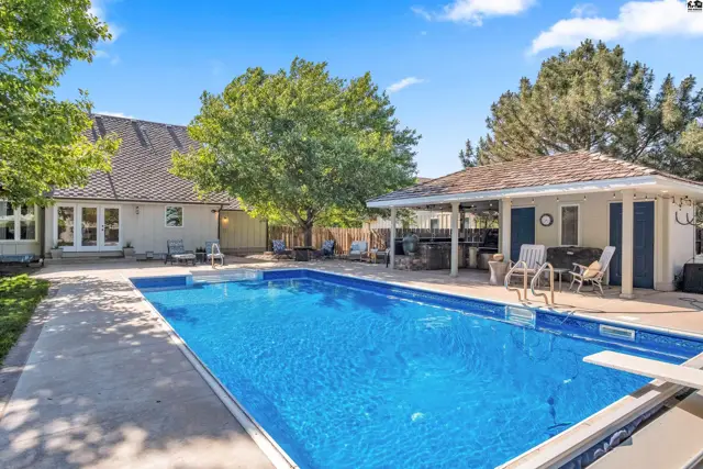 Spacious backyard features a sparkling blue swimming pool and a covered patio with seating.