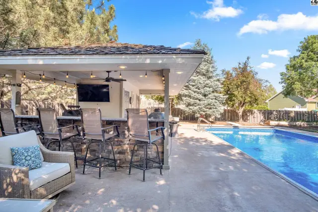 Covered outdoor bar with seating and a swimming pool in a sunny backyard.