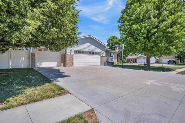Spacious driveway leads to a light gray home with a brick accent, two-car garage, and basketball hoop.