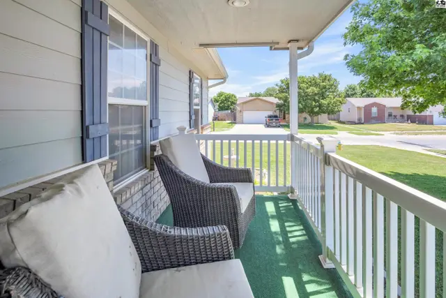 Covered front porch with wicker seating, white railing, and a green carpeted floor.