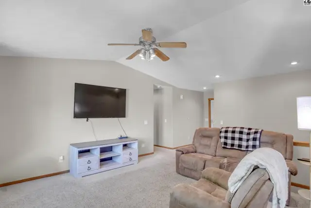 Spacious living room with vaulted ceilings, neutral carpet, and a mounted television above a white media console.