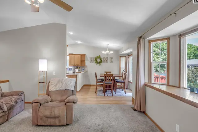 Spacious living area with plush seating, light wood floors, and a dining area visible through an open doorway.