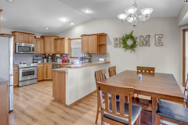 Spacious kitchen and dining area with light wood cabinets, stainless steel appliances, and a large wooden table.