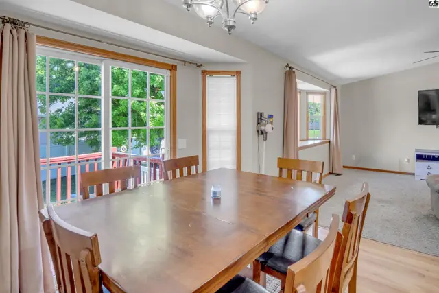 Wooden dining table and chairs in a bright room with large windows and sliding glass doors.