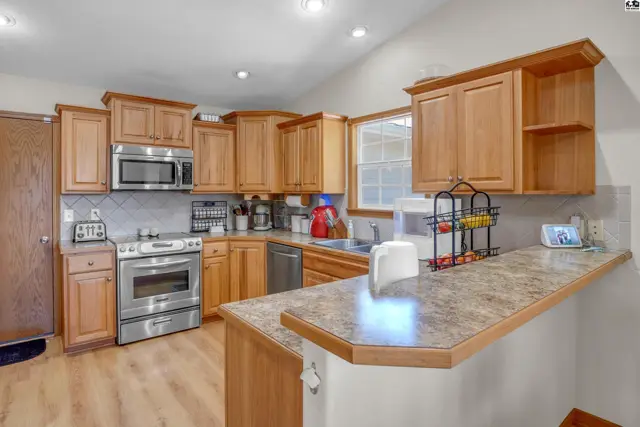 Spacious kitchen with light wood cabinets, stainless steel appliances, and a granite-look countertop.