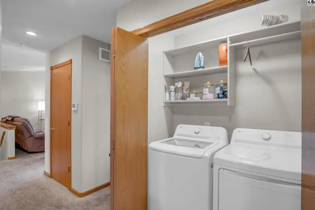 Laundry room with white washer and dryer, open shelving, and wood accents.