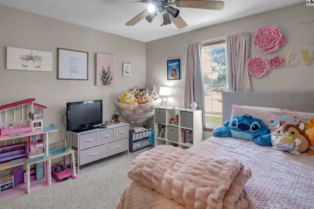 A child's bedroom with a bed, toys, and decorative pink flowers on a neutral-toned wall.