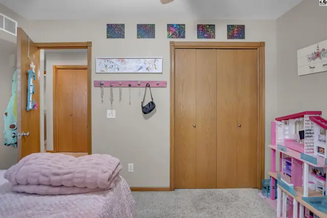 A child's bedroom features a pink bed, wooden closet doors, and a dollhouse.