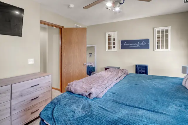Spacious bedroom with a large blue bed, light wood dresser, and ceiling fan.