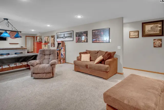 Spacious finished basement with a pool table, comfortable seating, and framed art on gray walls.