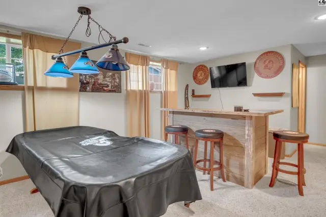 Finished basement recreation room with a covered pool table, bar with stools, and wall-mounted television.